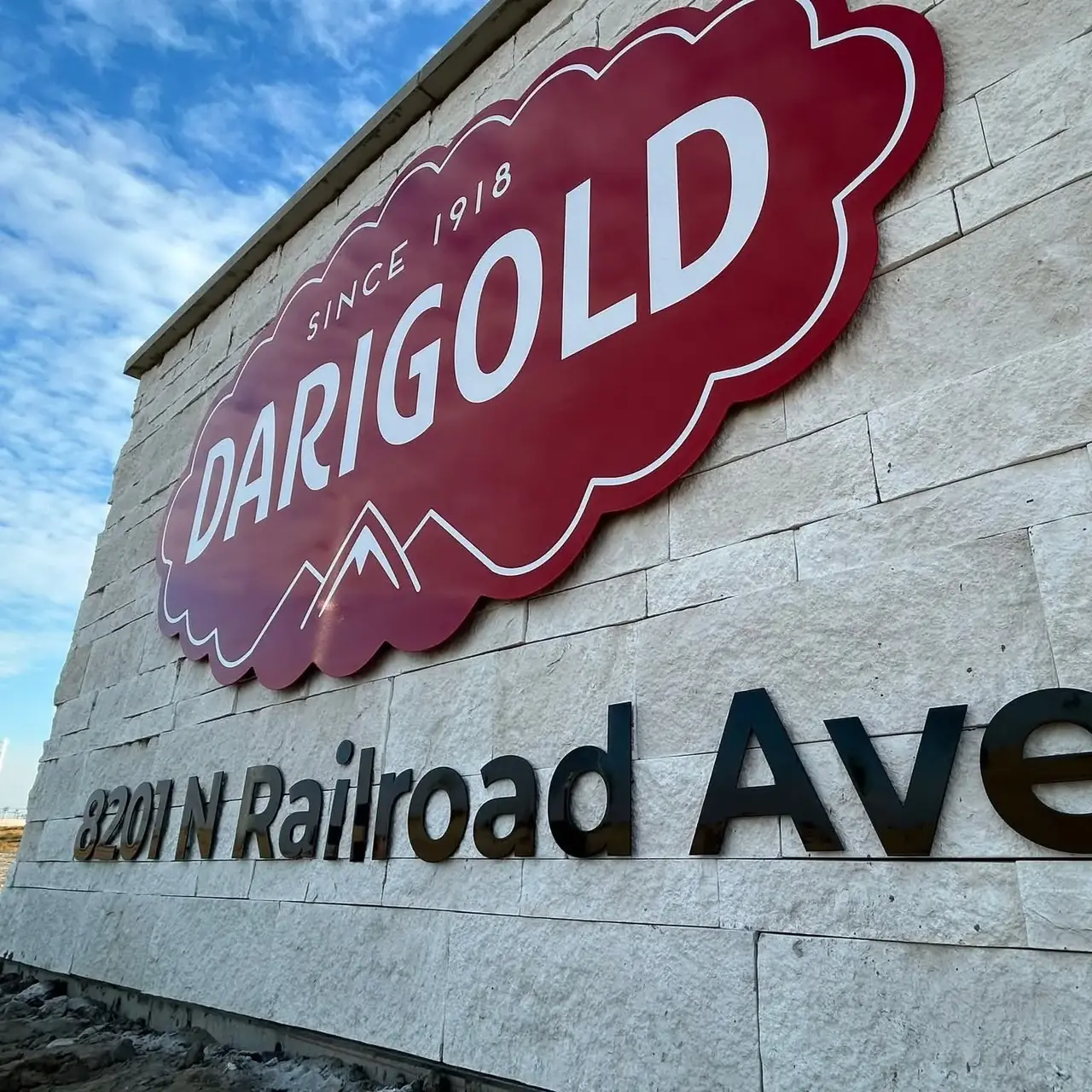 Burgundy Darigold sign and black address lettering installed on a pale stone wall