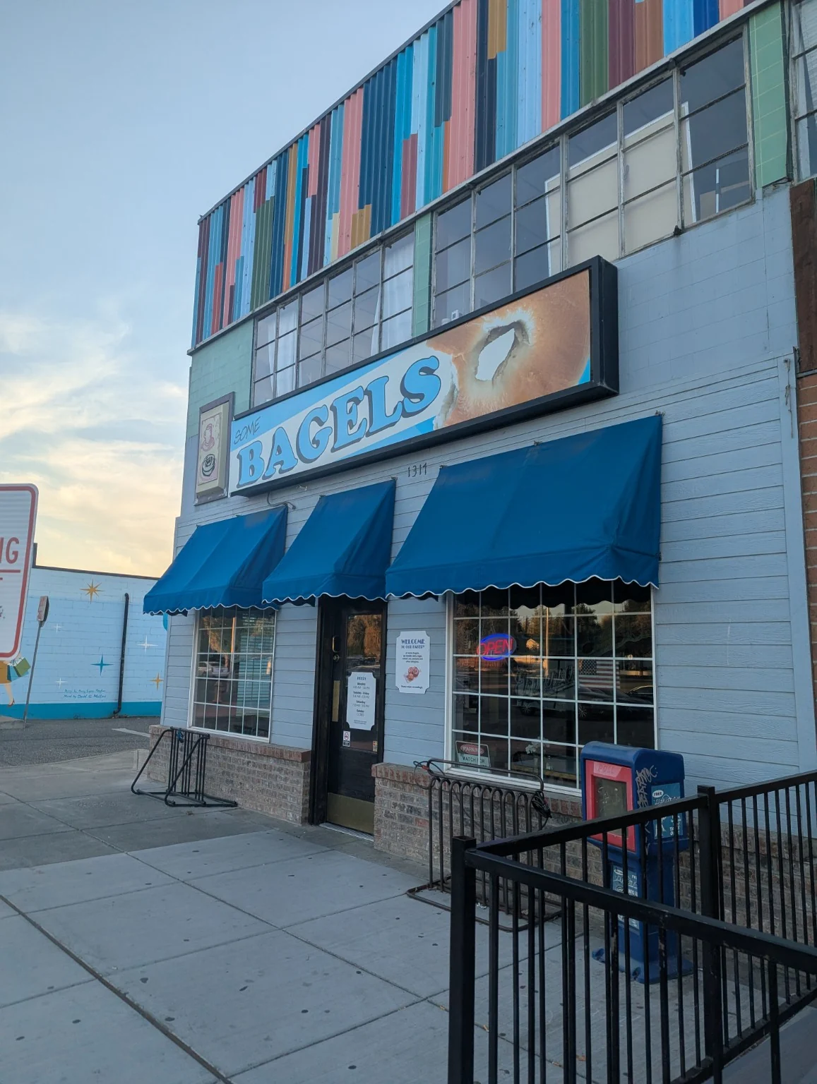 Some Bagels sign with blue lettering and bagel imagery above a storefront with blue awnings